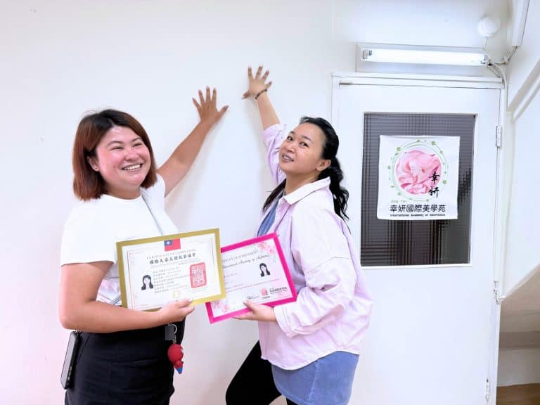 美甲全科班學員順利結業，與老師在教室門口開心擊掌慶祝，手持國際美容美體技藝協會證書與結業證書。